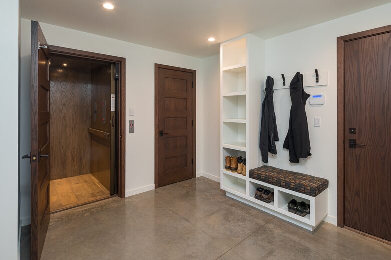 Bottom floor entryway with open elevator door and bench.